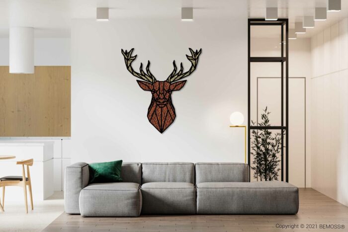 Een moderne woonkamer met een grijze bank versierd met een groen kussen. Boven de bank hangt een geometrisch kunstwerk van een hertenkop. De kamer heeft witte muren, lichte houten accenten, een klein verticaal raam en een minimalistische inrichting. Links is een deel van de keuken zichtbaar met daarin een BEMOSS moschilderij.