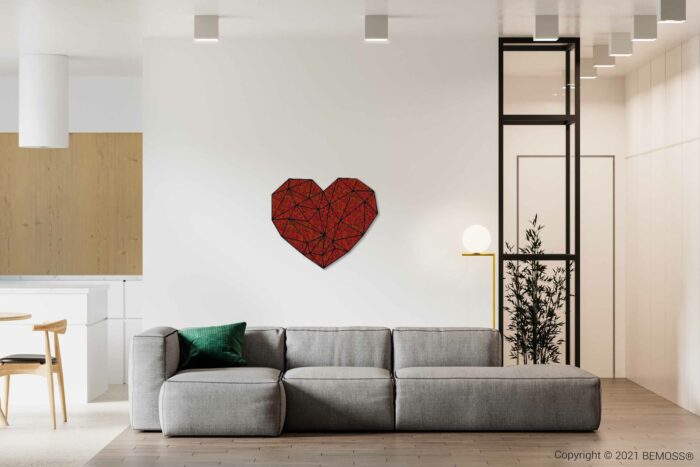 Moderne woonkamer met een grijze bank met een groen kussen, geometrische kunst aan de muur met een rood hart en een minimalistische inrichting. Een BEMOSS moschilderij geeft een organische toets aan de ruimte. Er is ook een eethoek met houten stoelen en een witte tafel op de achtergrond, en een hoge plant bij een glazen scheidingswand.