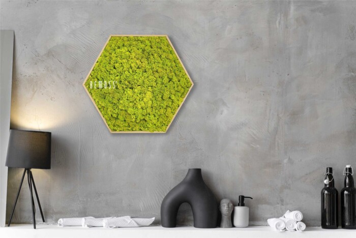 Een modern interieur bestaat uit een BEMOSS-mosschilderij die boven een minimalistisch aanrecht hangt met enkele kleine decoritems, waaronder een zwarte vaas, een zeepdispenser, opgevouwen witte handdoeken en twee zwarte waterflessen. Links staat een zwarte vloerlamp.