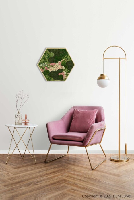 Een minimalistisch interieur bestaat uit een moderne plantenbak met BEMOSS moschilderij en roze bloemen in een zeshoekig frame op een witte muur. Hieronder staat een roze accentstoel met een bijpassend kussen naast een goud-witte bijzettafel. Rechts staat een gouden vloerlamp die het tafereel verlicht.