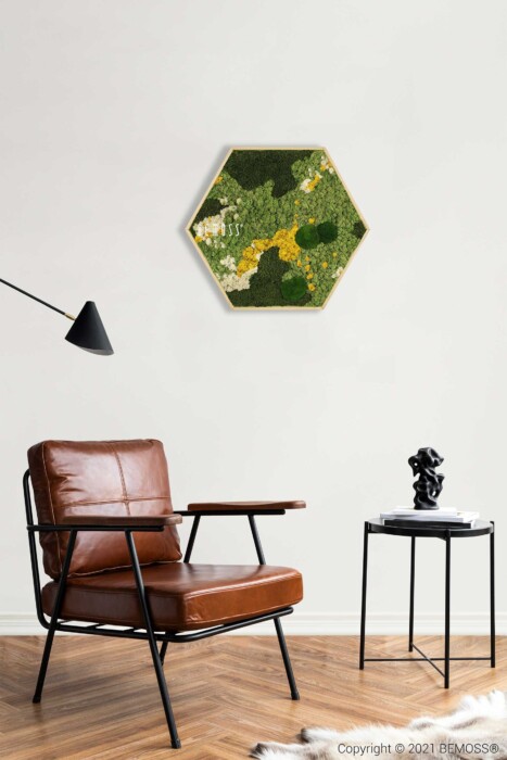 Een moderne woonkamer is voorzien van een bruinleren fauteuil met een zwart metalen frame, een klein zwart bijzettafeltje met een zwart decoratief beeldhouwwerk en een zeshoekige groene BEMOSS-mosschilderij aan de muur. De vloer is van hout met een wit tapijt en boven de stoel zweeft een zwarte wandlamp.