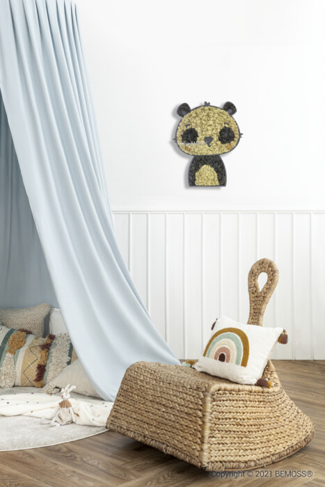 Een gezellige kinderkamer met een lichtblauwe gordijnhemel boven een speelhoek met kussens en een knuffelkonijn. Vlakbij staat een kleine rieten stoel met een regenboogkussen. De muur is versierd met een BEMOSS-pandabeerdecoratie gemaakt van natuurlijke materialen, wat een milieuvriendelijk tintje geeft aan de serene ruimte.