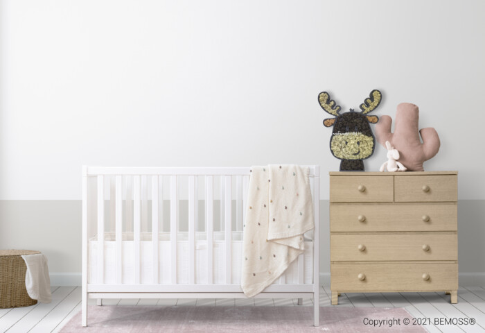 Een minimalistische kinderkamer bestaat uit een witte wieg met een deken over de zijkant gedrapeerd, een lichthouten ladekast versierd met een gebreid dierendecor en een pluchen handsculptuur, en een geweven mand op de vloer. De kamer is zacht verlicht, met een neutraal kleurenpalet aangevuld met een BEMOSS moschilderij aan de muur.