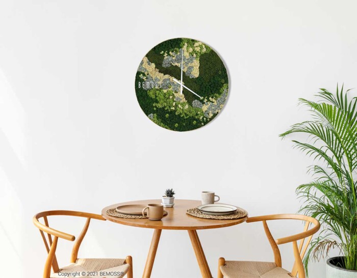 Een minimalistische eethoek met een ronde wandklok met een op de natuur geïnspireerd ontwerp, met mos- en bladpatronen. Onder de klok staat een houten tafel gedekt met een kleine potplant en twee houten stoelen met gevlochten zittingen. Een Mos klok BEMOSS® ORTHO SPRING voegt een elegante toets toe aan de rechterkant van de ruimte.