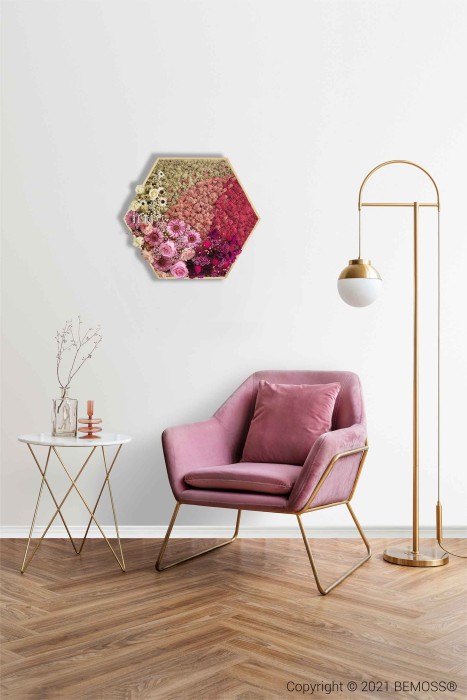 Een stijlvolle woonruimte met een roze fluwelen fauteuil met gouden poten, een moderne witte bijzettafel met een vaas en glaswerk, en een elegante vloerlamp met een gouden frame en witte kap. Achter de fauteuil aan de muur bevindt zich een zeshoekige Mosschilderij PLANTEN Cupido die de natuurlijke esthetiek versterkt.