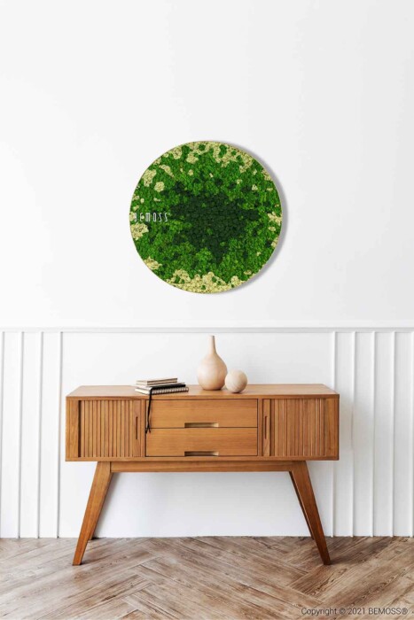 Een moderne houten consoletafel uit het midden van de eeuw met lades aan de voorkant staat tegen een witte muur. Daarboven hangt een ronde BEMOSS-mosschilderij. Op de tafel staan twee minimalistische beige vazen en een gesloten boek. De vloer is voorzien van een visgraatmotief.