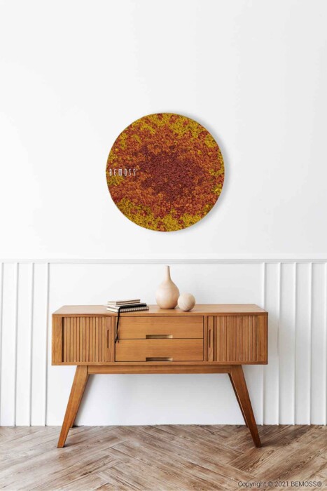 Een minimalistische kamer met een houten consoletafel met een geribbelde voorkant, waarop twee vazen van klei en een boek staan. Boven de tafel hangt een rond, rood en geel getextureerd kunstwerk aan de muur. De witte wand is voorzien van lambriseringen, aangevuld met een BEMOSS moschilderij en de vloer heeft een visgraatmotief.