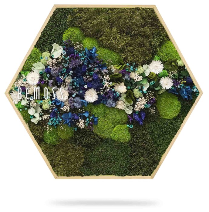 Een hexagonaal houten frame bevat een groen en wit bloemstuk. Het ontwerp bevat mos, witte en blauwe bloemen en groen. Het woord 