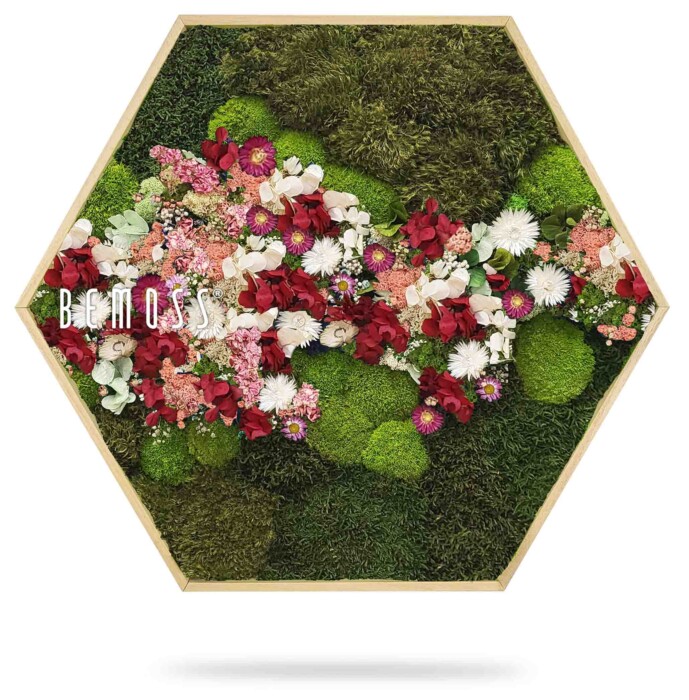 De Moshexagon PLANTEN Acebo (Kópia) heeft een zeshoekig houten frame met een arrangement van groen mos versierd met trossen rode, witte en roze kunstbloemen. De inscriptie 